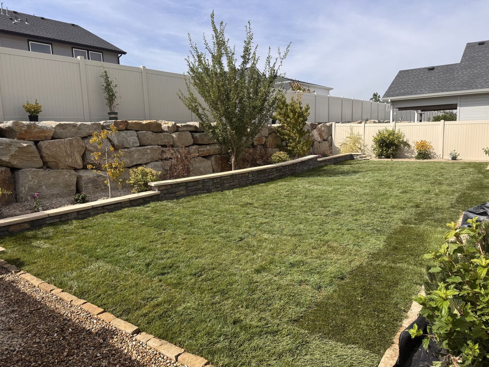 Finished backyard with stacked stone retaining wall, capstones, and fresh sod lawn