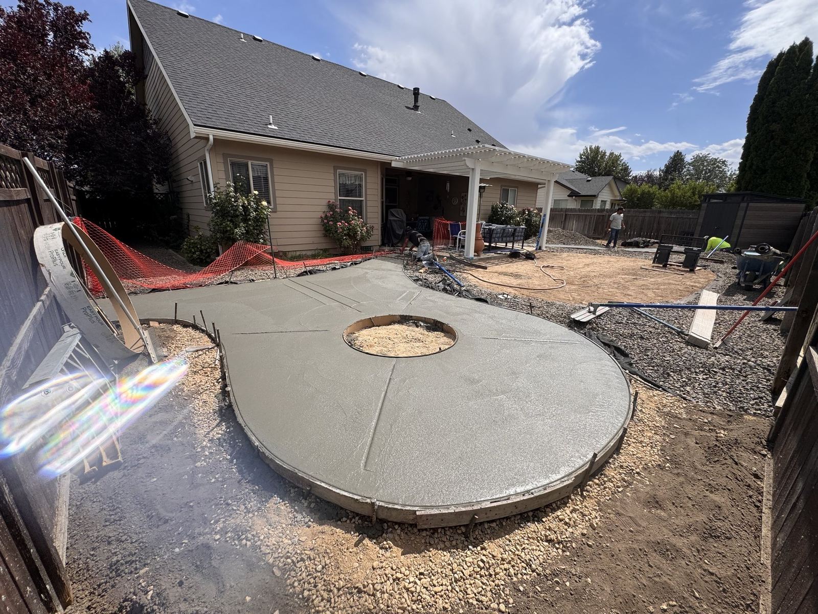 Stamped concrete patio being formed and poured with a central fire-pit cutout, pergola in background