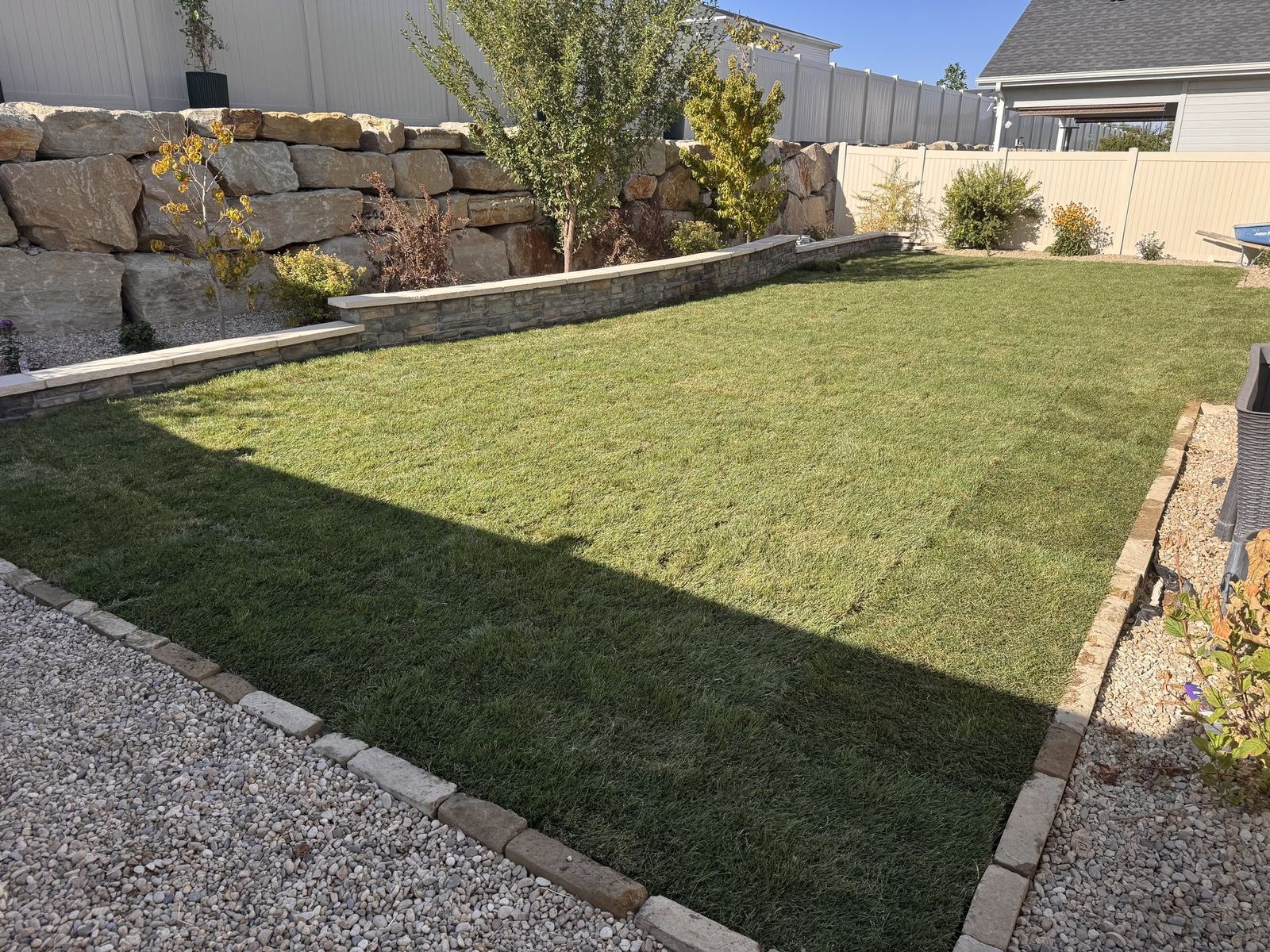 Finished backyard with stacked stone retaining wall, boulder-wall accents, fresh sod lawn, and cobblestone border